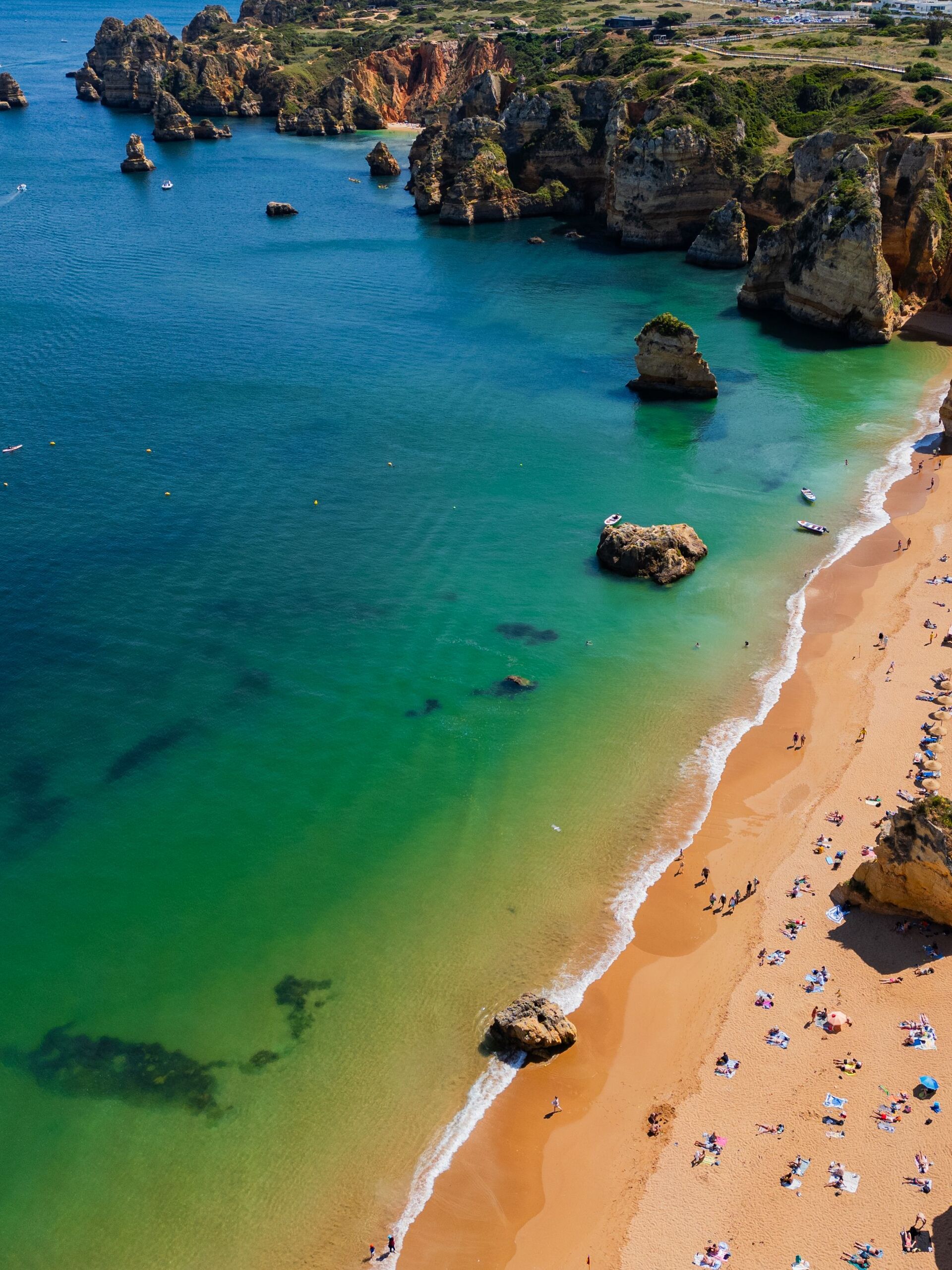 Aerial view of a golden Lagos beach meeting green-blue water and rock stacks
