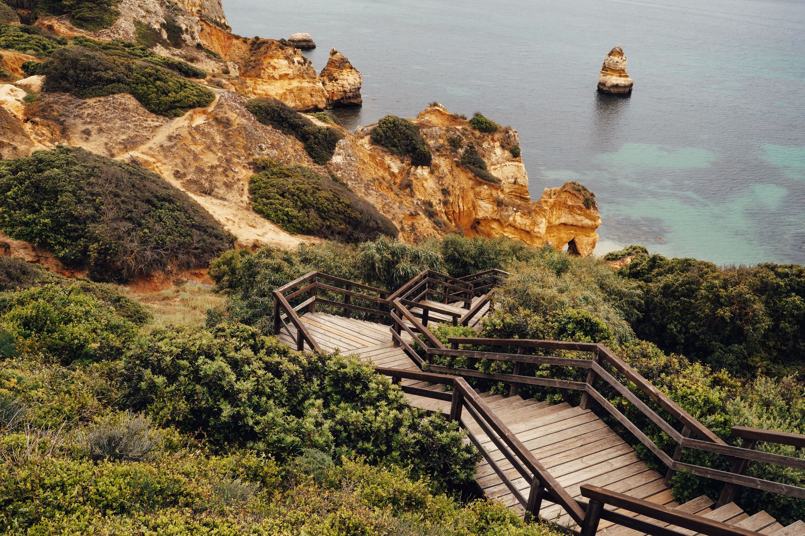 A wooden boardwalk winding down through greenery to the Lagos cliffs and sea