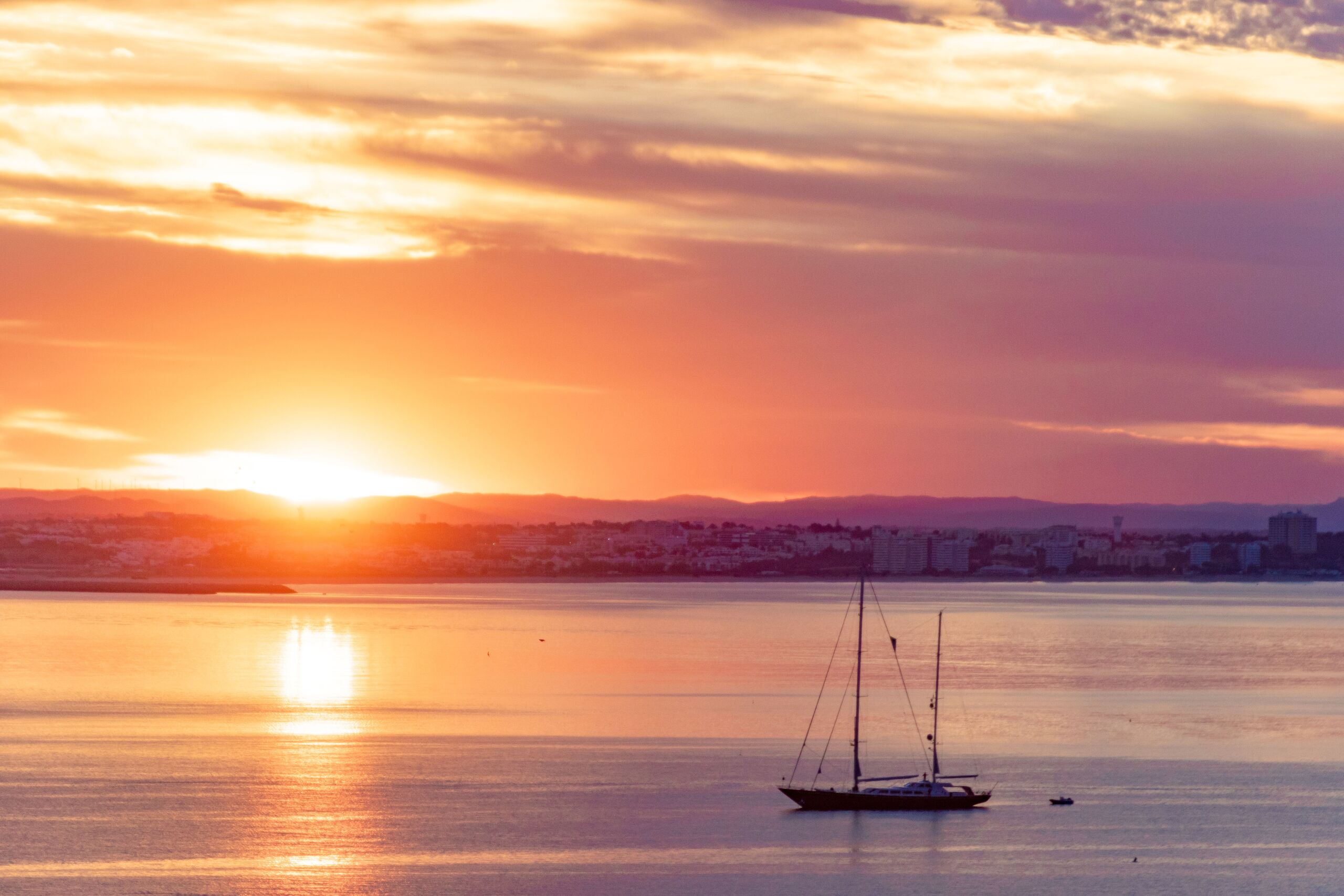 Sunset over Lagos bay with a sailboat resting on calm, golden water